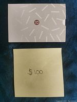 Top view of the Lululemon branded envelope lying on a dark blue surface with a yellow sticky note showing handwritten '$100'.