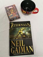 Lot overview showing Eternals book, Infinity Gauntlet toy in packaging, and vintage Marvel coffee mug.
