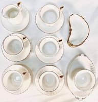 Top view of tea set pieces including 5 cups, 6 saucers, and 4 side trays displaying shape and gold trim detail.