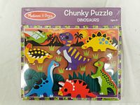 Front of the Melissa and Doug Chunky Puzzle box showing colorful dinosaur puzzle pieces inside package wrap.