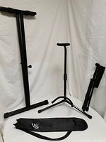 Overall view of keyboard stand, guitar stand, foldable music book stand and carrying case, against white fabric background