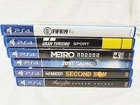 Stack of six PlayStation 4 game cases showing titles and artwork on spine: FIFA 19, Gran Turismo Sport, Metro Exodus, Just Cause 3, InFamous Second Son, Batman Arkham Knight.
