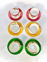 Top view of six tea cups placed on matching saucers, showing the red, yellow, and green colored borders and floral interior designs.