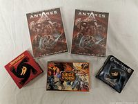 Photo showing all five games arranged: two Antares The Dice Game boxes, one Siege Storm card game, and two Werewolves games (The Werewolves of Millers Hollow and New Moon Expansion).