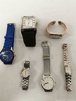 Collection of six diverse wristwatches including multiple band materials and case shapes laid on white background