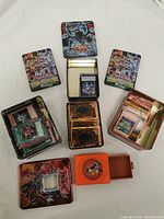 Four Yu-Gi-Oh card tins arranged with one open showing cards inside, plus an orange card holder.