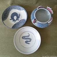 Three pottery bowls with animal motifs: snake, rabbit, peacock, displayed together on green fabric