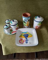 Photo showing 8 piece pottery set including lidded jars on tray, tall vase, lidded jar, and square platter with fruit and flower artwork.
