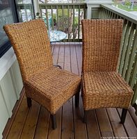 Pair of traditional seagrass chairs shown on a wooden deck, with woven seagrass seats and backs and dark wood legs.