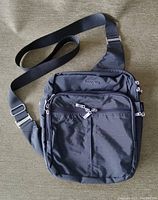 Front view of black Baggallini crossbody bag showing multiple front zippered compartments and adjustable strap.