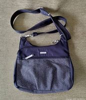 Front view of Baggallini women's criss-cross bag showing black and gray fabric, adjustable strap, and front zipper pocket.