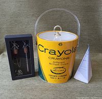 Photo showing all three items together: Crayola ice bucket with clear acrylic handle, black box with pewter bar tools, and white pyramid candle