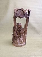 Front view of the wood carving showing the seated violin player detailed with a hat and bow.