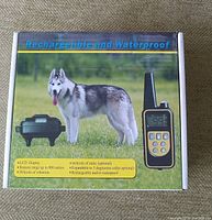 Box with product information showing a picture of a husky and remote control, highlighting rechargeable and waterproof features, LCD display, 800 meters range, 99 vibration levels, and expandable to 3 dogs.