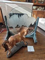 Etched glass disk with draught horses in wooden stand and carved wooden horse on table