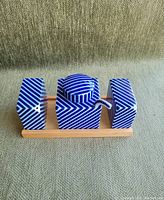 Porcelain condiment set items arranged on wooden tray showing salt shaker, soy sauce pot with lid and spout, and pepper shaker, all decorated in blue and white diagonal stripes.