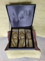 Opened box with three carved Buddha candles inside, showing texture and fabric lining on lid