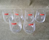 Six clear stemless wine glasses arranged on fabric surface, each with red Spiegelau logo sticker, showing set quantity and condition.