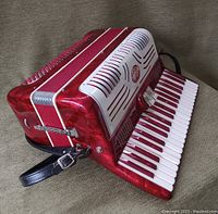 Side view of the red marbled Salanti accordion showing the keyboard, grille, emblem, and leather strap attachment.