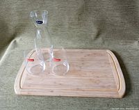 Overall lot: bamboo cutting board with two Spieglau glasses and Italian carafe arranged for display.