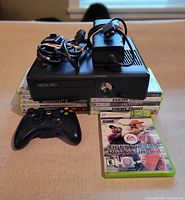 Xbox 360 console with power pack, cords, and controller on stack of game cases showing part of the lot contents.
