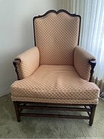 Front view of a wingback chair with peach and beige patterned fabric upholstery, dark wood frame and legs