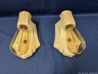 Front view of the pair of beige ceramic lamp sconces with attached Edison bulbs side by side on blue cloth.