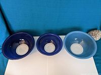 Front view of 3 Pyrex blue bowls of varying shades and sizes on white surface with blue cloth background.