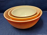 Stacked view of 3 nested Pyrex bowls showing orange exterior and white interior with visible wear marks on the largest bowl.