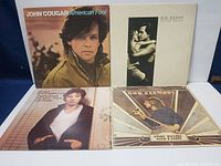 Four vinyl record album covers including John Cougar's "American Fool," Bruce Springsteen's "Born to Run," and two Rod Stewart albums: "Greatest Hits Classic Edition" and "Every Picture Tells a Story."