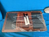 Overview of the entire charcuterie board showing the wooden construction, two black stone inserts, and the utensils in the center slots covered with plastic.