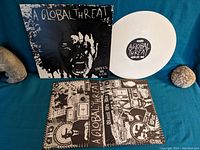 Photo showing white vinyl record and album cover sleeve with aggressive graphic art and text 'A Global Threat Until We Die'.