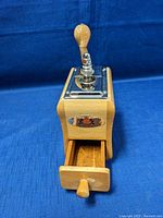 Front angled view showing wooden drawer open and metal top with hand crank.