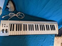 Full top view of the M-Audio KeyRig 49 keyboard showing keys, pitch/mod wheels, USB cable, and controls.