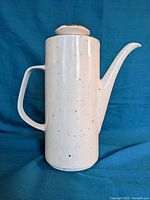 Front side view of a tall white ceramic coffee pot with black speckles, cylindrical body, angular handle, and narrow spout with lid.