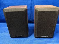 Front view of the pair of black grille Technics speakers on wooden cabinets.
