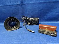 Lens, camera and rangefinder meter arranged on blue cloth background.
