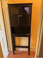 Front view of tall black laminate cabinet with two glass-paneled doors and an open shelf below.