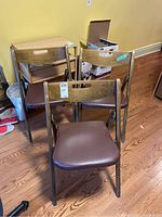 Three foldable wooden chairs with brown faux leather seat cushions arranged in a group, showing front and side views.