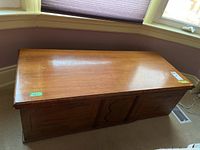Front view of the wooden chest showing the smooth lid surface with scratches and paneled door fronts.