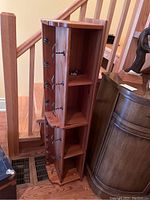 Wooden coat rack positioned in corner near staircase, showing its tall vertical shape with hooks and shelves