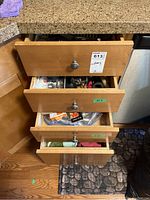 Image showing several kitchen drawers partially open filled with various kitchen utensils and cutlery including forks, knives, spoons, and some handles of different kitchen tools.