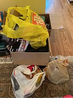 Box containing a yellow plastic bag and a white plastic bag filled with light bulbs, sitting on a carpeted floor.