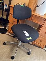 Front view of black office chair showing foam seat and backrest, metal base, and casters.