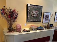 Full view of console table with various decorative items including vase with faux flowers, salt lamp, dessert platter, coasters, framed artworks and figures.