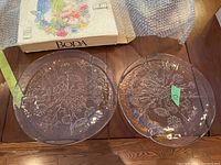Two clear glass platters with floral etching on surface shown on wooden table with bubble wrap.
