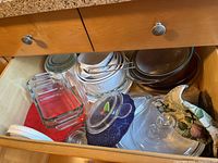 Drawer containing assorted glass Pyrex bakeware including clear rectangular baking dishes with lids, round bowls and ramekins