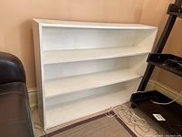 Front view of white painted wooden shelf showing three shelves and paint finish.
