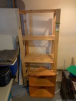 View of the two shelving units together, larger rectangular shelf with three slatted wooden shelves and smaller triangular corner shelf stacked in front.