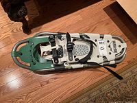 Front top view of one snow shoe showing green aluminum frame, bindings, and foot bed grip area.